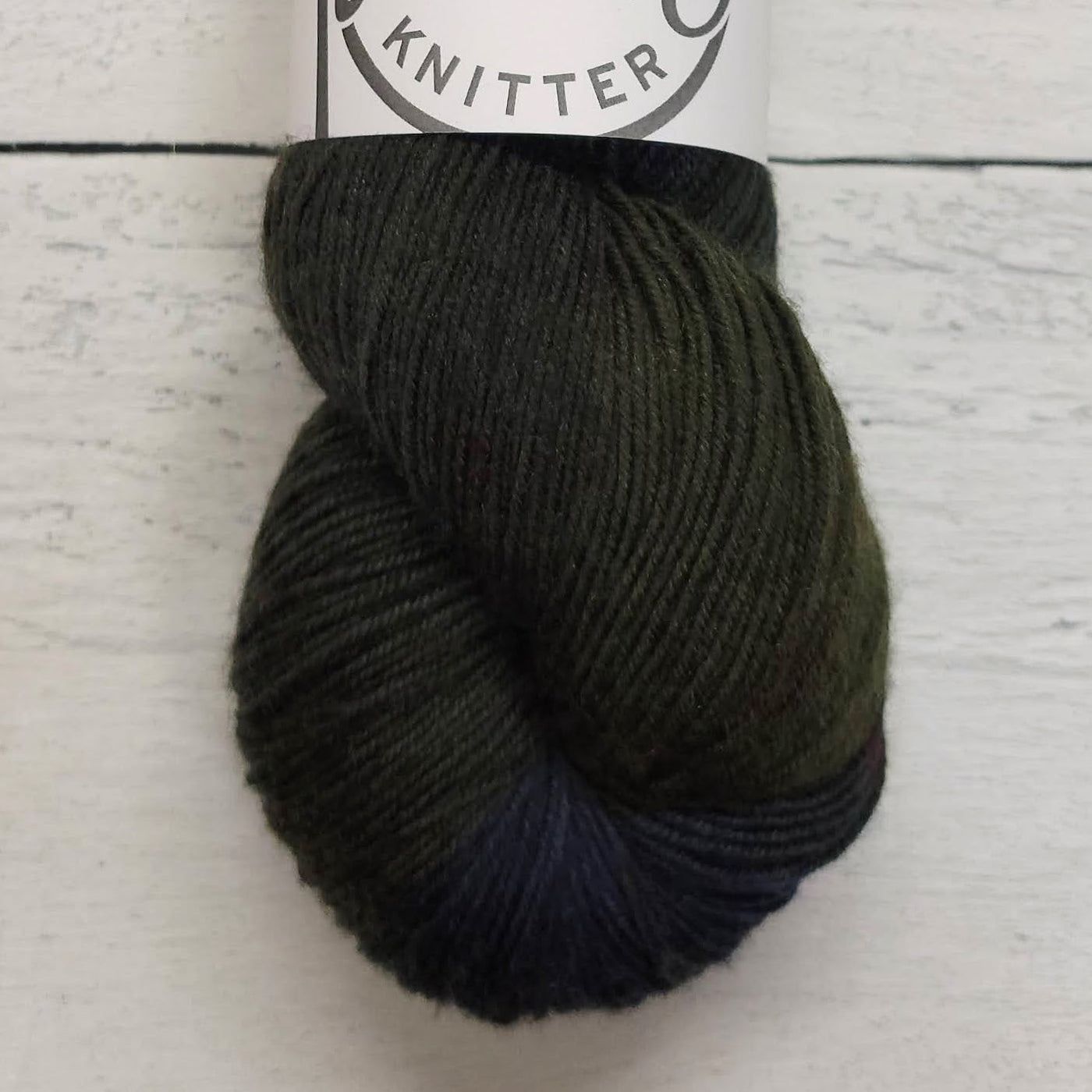 Ball of dark yarn with a label on a light wooden surface
