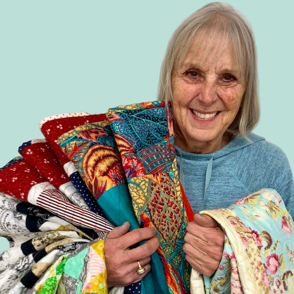 An older woman smiling and holding a bundle of colorful fabric, likely created during a quilting or sewing class.