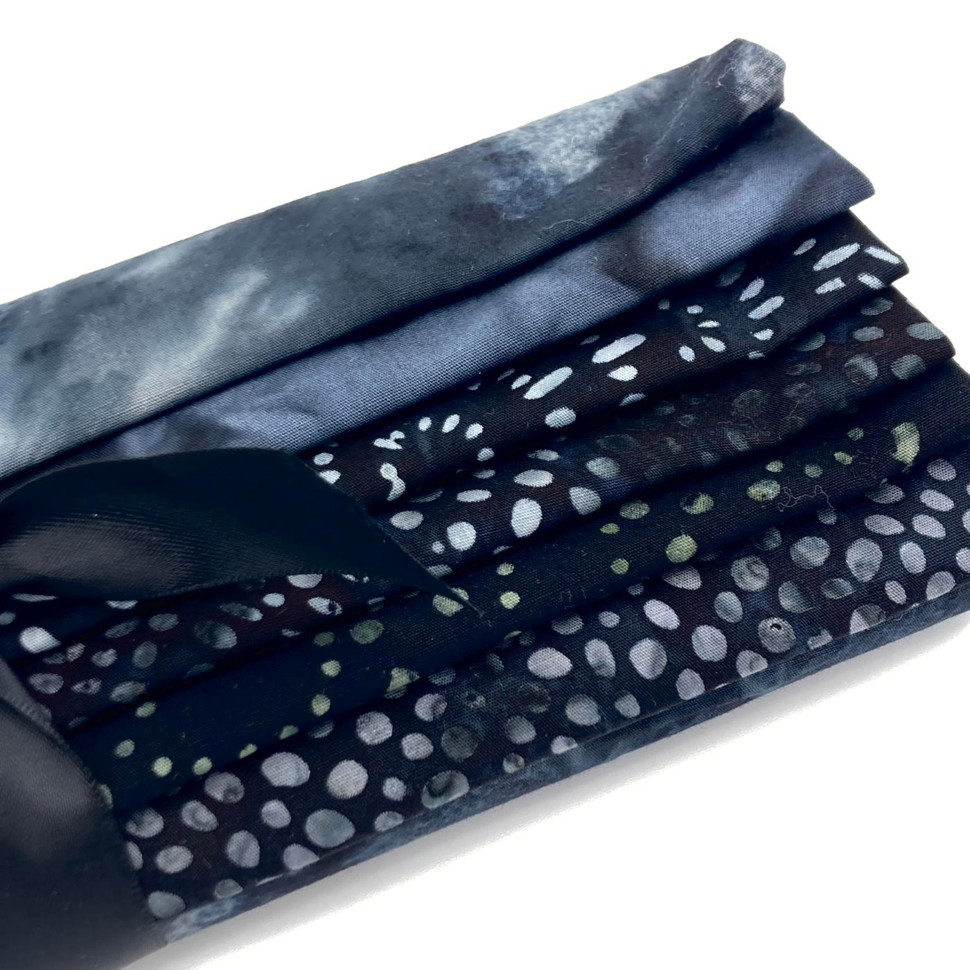 Six different grey and dark grey toned batik fabric fat quarters in a bundle tied with a black ribbon.