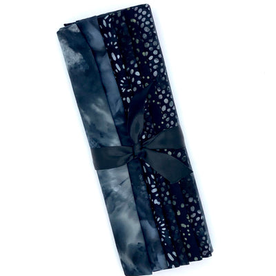 Six different grey and dark grey toned batik fabric fat quarters in a bundle tied with a black ribbon.