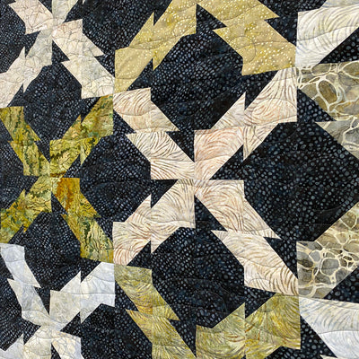 Quilt with geometric pattern in black, white, and gold on a dark background