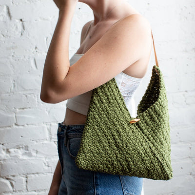 Person holding a green knitted bag against a white brick wall