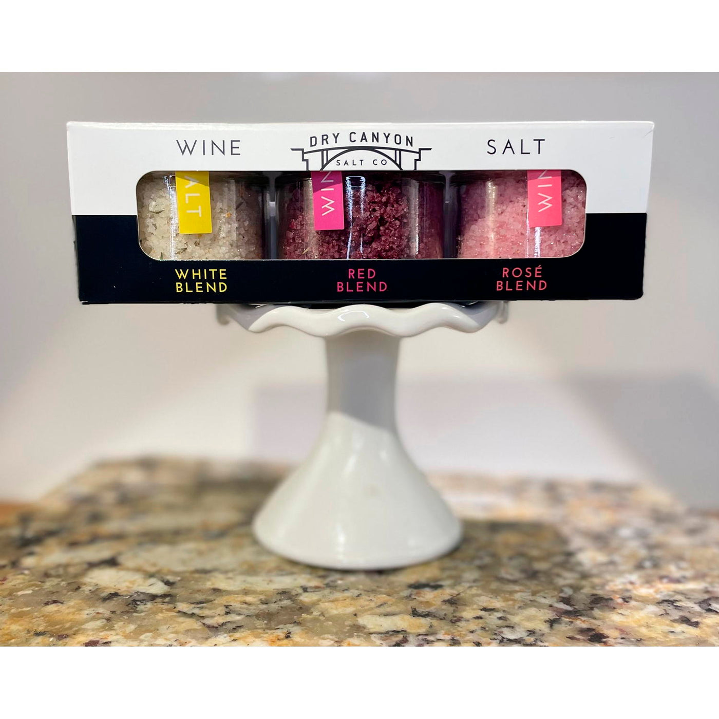 Packaged salt with wine flavorings on a white pedestal stand against a neutral background