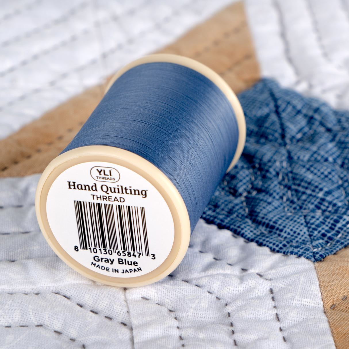Spool of gray blue hand quilting thread on a quilted fabric background