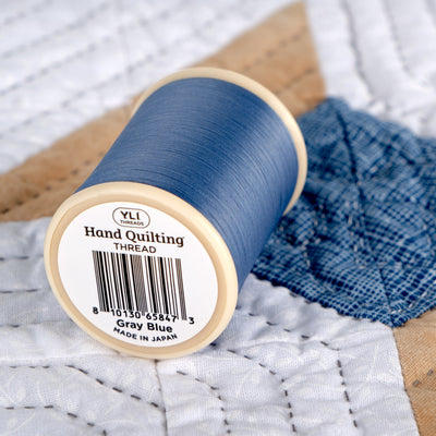 Spool of gray blue hand quilting thread on a quilted fabric background